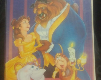 Puede incluir: Una caja de cinta VHS con la película clásica de Disney "La Bella y la Bestia". La portada muestra a Bella y la Bestia bailando, con otros personajes como Lumière, Din Don y la Señora Tetera en el fondo.