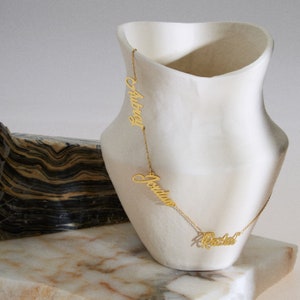 May include: Gold necklace with three personalized nameplates: Aubrey, Jonathan, and Rachel.