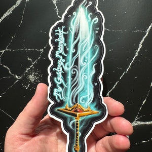 May include: A sticker of a glowing blue sword with a gold hilt and a red gem. The sword is surrounded by blue flames and the text "My Guiding Moonlight" is written on the side.