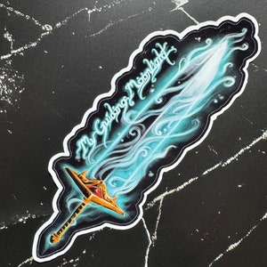 May include: A sticker featuring a blue and gold sword with a white outline. The sword is surrounded by a blue and white swirl. The text "The Guiding Moonlight" is written in a cursive font above the sword.