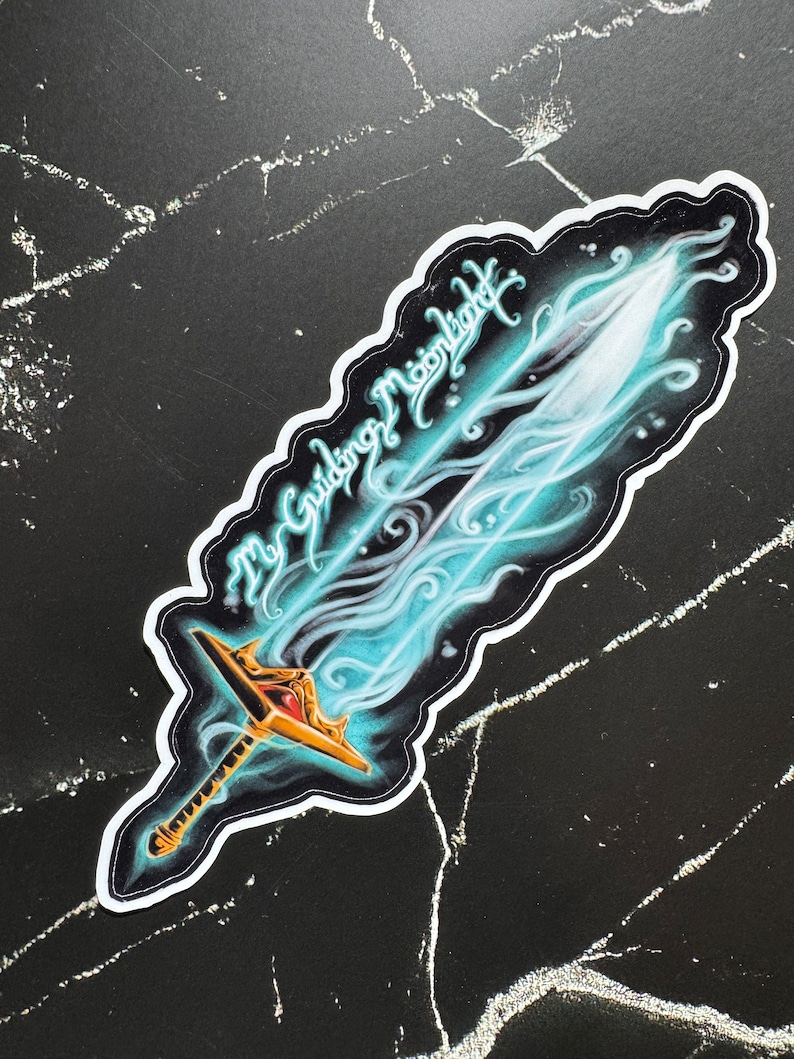 May include: A sticker featuring a blue and gold sword with a white outline. The sword is surrounded by a blue and white swirl. The text "The Guiding Moonlight" is written in a cursive font above the sword.