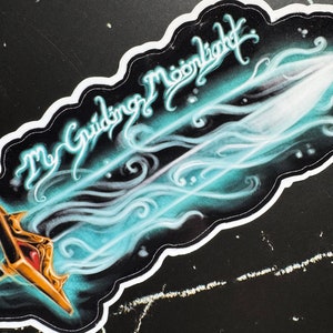 May include: A sticker featuring a blue and white sword design. The sword is surrounded by a swirling, smoky effect. The text "The Guiding Moonlight" is written in a stylized font above the sword.
