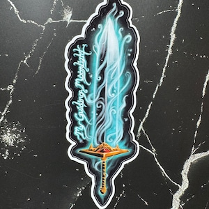 May include: A sticker of a glowing blue sword with a gold hilt and a red jewel. The sword is surrounded by blue flames and the text "My Guiding Moonlight" is written on the side.