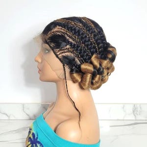 May include: A side profile of a mannequin head wearing a braided wig. The wig features a combination of black and brown braids, with the ends styled into voluminous, golden-brown curls. The wig is secured with a lace front.
