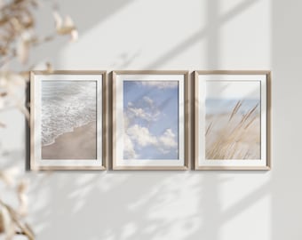 Peut inclure: Trois impressions encadrées avec des scènes de plage. L'impression de gauche montre un gros plan de vagues mousseuses sur une plage de sable. L'impression du milieu montre un ciel bleu avec des nuages blancs. L'impression de droite montre de hautes touffes d'herbe qui soufflent dans le vent.