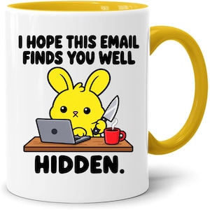 May include: A white ceramic mug with a yellow interior and handle, featuring a graphic of a yellow bunny at a desk with a laptop, a red mug, and a knife. The text reads: I HOPE THIS EMAIL FINDS YOU WELL HIDDEN. The design is centred on the mug.