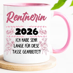 May include: White ceramic mug with a pink interior and handle. The mug features the text "Rentnerin 2026" in pink script, along with the phrase "ICH HABE SEHR LANGE F&Uuml;R DIESE TASSE GEARBEITET!" in black, and floral accents.