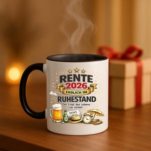 May include: A white ceramic mug with a black handle and rim. The mug features the text "RENTE 2026 ENDLICH IM RUHESTAND" in gold lettering, along with illustrations of beer, a bottle, a hat, and a clock. The mug is a retirement gift.