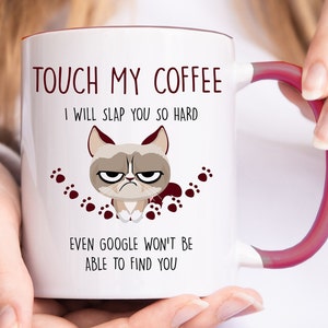 Op de afbeelding: Witte keramische koffiemok met een rode handgreep. De mok heeft een cartoonafbeelding van een chagrijnige kat met de tekst "TOUCH MY COFFEE I WILL SLAP YOU SO HARD EVEN GOOGLE WON'T BE ABLE TO FIND YOU".