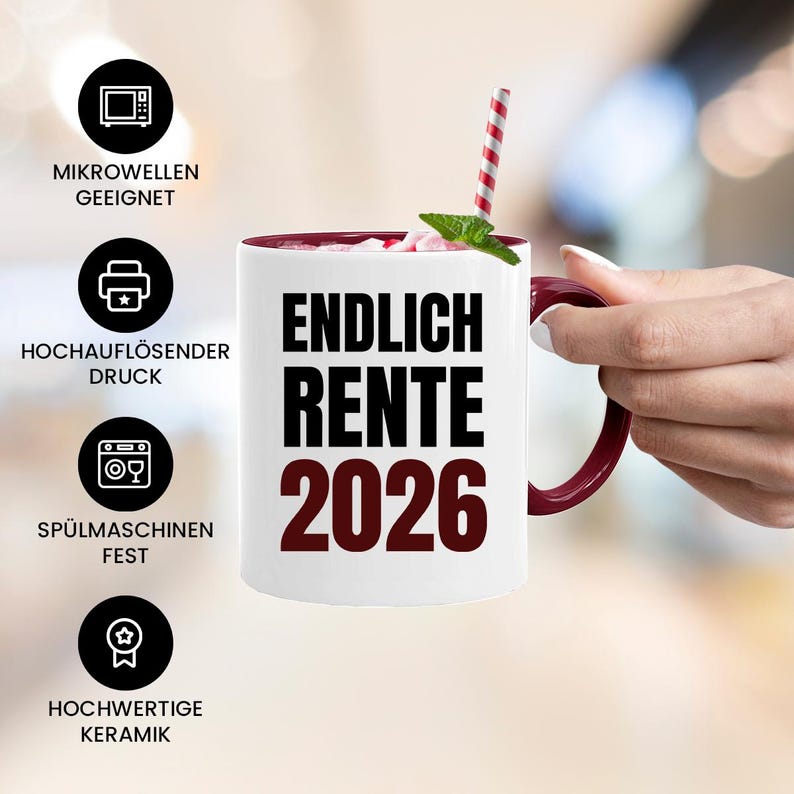 May include: White ceramic mug with a burgundy interior and handle. The mug features the text "ENDLICH RENTE 2026" in black and burgundy. A red and white striped straw and a sprig of mint are visible. The mug is held by a person.