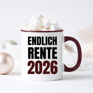 May include: White ceramic mug with a burgundy rim and handle, filled with marshmallows. The mug features the text "ENDLICH RENTE 2026" in black and burgundy lettering. A festive and celebratory design.
