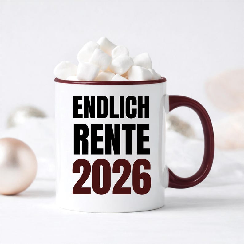 May include: White ceramic mug with a burgundy rim and handle, filled with marshmallows. The mug features the text "ENDLICH RENTE 2026" in black and burgundy lettering. A festive and celebratory design.
