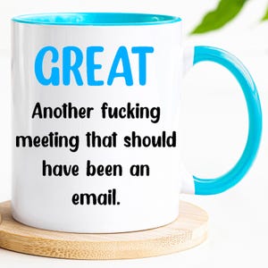 Könnte beinhalten: Weiße Keramik-Tasse mit blauem Innenraum und Henkel, mit dem Wort "GREAT" in Blau. Die Tasse trägt die Aufschrift "Another fucking meeting that should have been an email."