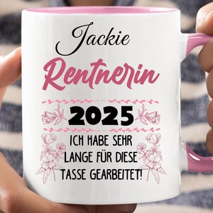 Puede incluir: Taza de cer&aacute;mica blanca con interior y asa rosas. La taza presenta el nombre "Jackie" en escritura negra, la palabra "Rentnerin" en escritura rosa, el a&ntilde;o "2025" y una frase alemana en texto negro.