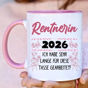 May include: White ceramic mug with a pink interior and handle. The mug features the text "Rentnerin 2026" in pink script, with additional text below. Floral accents surround the text.