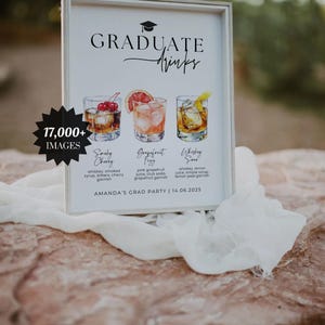 May include: A framed sign with the words "GRADUATE Drinks" and illustrations of three cocktails: Smoky Cherry, Grapefruit Fizz, and Whiskey Sour. The sign includes the text "AMANDA'S GRAD PARTY | 14.06.2025".