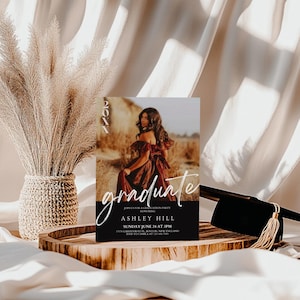 Op de afbeelding: Een zwart-witte uitnodiging voor een afstudeerfeest met een foto van een vrouw in een rode jurk. De tekst op de uitnodiging luidt "graduate" in wit handschrift en "Ashley Hill" in witte blokletters. De datum en tijd van het feest staan hieronder vermeld.
