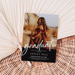Op de afbeelding: Een zwart-witte uitnodiging voor een afstudeerfeest met een foto van een vrouw in een bruine jurk. De tekst op de uitnodiging luidt "graduate", "Join us for a graduation party", "Ashley Hill", "Sunday June 24 at 3PM", "1212 Cambridge St, Boston, MA 02139", "RSVP to Camila at 123-456-7890".