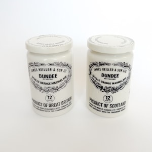 Puede incluir: Dos tarros de cerámica blancos de mermelada de naranja de Sevilla Dundee. Cada tarro tiene una etiqueta en blanco y negro con texto y un borde decorativo. Los tarros están etiquetados como "Product of Great Britain" y "Product of Scotland."