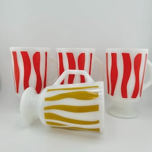May include: Four vintage milk glass mugs with a footed base. Three mugs have red and white wavy stripes and one mug has gold and white wavy stripes.