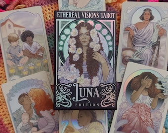 May include: A spread of tarot cards from the Ethereal Visions Tarot Luna Edition deck. The cards feature illustrations of people and scenes in a whimsical style. The cards are laid out on a colorful knitted blanket.
