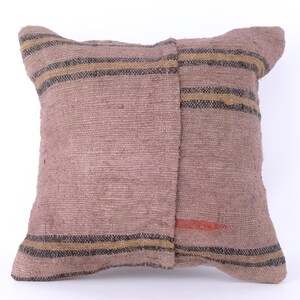 Puede incluir: Una almohada de tiro de rayas marrones y beige con una tela tejida texturizada. La almohada tiene una sutil mancha roja en la parte posterior.