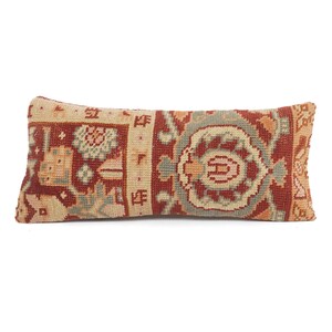 May include: Rectangular decorative pillow with a detailed, vintage-style pattern. The pillow features a beige background with a repeating design in shades of red, blue, and orange. The pillow is a long, bolster shape.