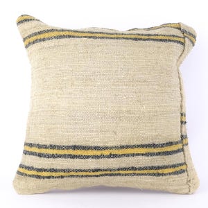 Puede incluir: Una almohada beige con rayas amarillas y negras. La almohada está hecha de un tejido tejido y tiene una superficie ligeramente texturizada.