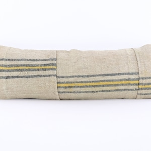 May include: A long, rectangular cushion with a beige linen fabric cover. The cushion has black and yellow stripes running horizontally across the fabric.