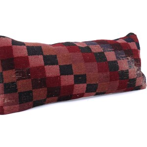 May include: Rectangular pillow with a checkered pattern in shades of red, black, and brown. The pillow has a textured surface and a slightly worn appearance, suggesting it may be vintage or handmade. The pillow is designed for decorative use.