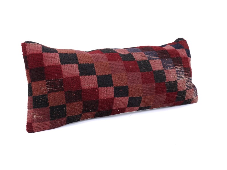 May include: Rectangular pillow with a checkered pattern in shades of red, black, and brown. The pillow has a textured surface and a slightly worn appearance, suggesting it may be vintage or handmade. The pillow is designed for decorative use.