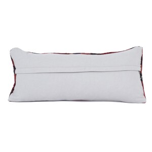 May include: Rectangular pillow with a white back and a patterned front. The front features a design with red, black, and white colors. The pillow is a decorative item, likely for a sofa or bed.