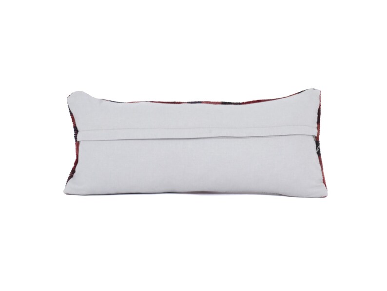 May include: Rectangular pillow with a white back and a patterned front. The front features a design with red, black, and white colors. The pillow is a decorative item, likely for a sofa or bed.