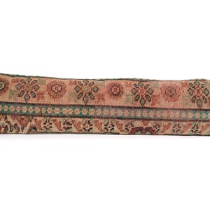 May include: A long, rectangular pillow with a faded, vintage look. The pillow features a repeating floral pattern in shades of peach, brown, and green, with a teal border. The pillow's design suggests a traditional or bohemian style.
