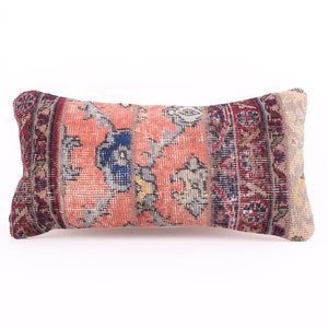 Puede incluir: Una almohada rectangular con un estampado floral colorido. La almohada está hecha de una tela tejida con un aspecto vintage. La tela es una mezcla de rojo, azul, rosa y beige.