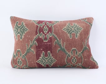 May include: A rectangular pillow with a red, green, and beige patterned design. The pillow is made of a woven fabric with a textured surface.