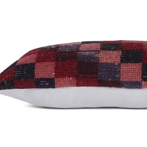 May include: A rectangular pillow with a checkered pattern in shades of red, burgundy, and navy blue. The pillow's base is a light gray color. The pillow is designed for decorative purposes.