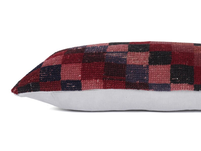 May include: A rectangular pillow with a checkered pattern in shades of red, burgundy, and navy blue. The pillow's base is a light gray color. The pillow is designed for decorative purposes.