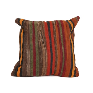 May include: A square throw pillow featuring a woven textile cover with vertical stripes in shades of brown, rust orange, olive green, black, and yellow. The fabric has a textured, coarse appearance with visible weave patterns throughout the surface.
