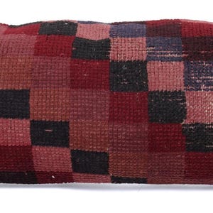 May include: A rectangular pillow with a patchwork design. The pillow features a pattern of squares in shades of red, black, and burgundy. The pillow is made of a textured fabric, and the design is symmetrical.