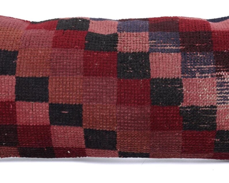 May include: A rectangular pillow with a patchwork design. The pillow features a pattern of squares in shades of red, black, and burgundy. The pillow is made of a textured fabric, and the design is symmetrical.