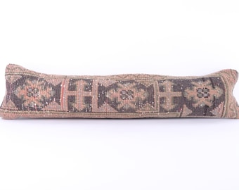 May include: A long, rectangular pillow with a traditional Turkish kilim pattern in shades of pink, brown, and green. The pillow is made from woven fabric and has a fringed edge.