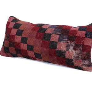 May include: Rectangular pillow with a checkerboard pattern in shades of red, black, and brown. The pillow has a textured appearance, suggesting a woven or embroidered design. The pillow is a decorative home accent.