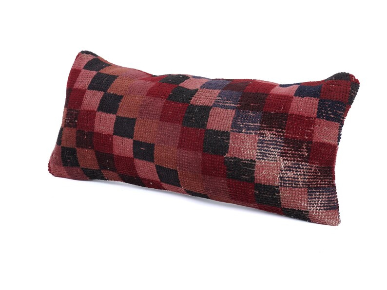 May include: Rectangular pillow with a checkerboard pattern in shades of red, black, and brown. The pillow has a textured appearance, suggesting a woven or embroidered design. The pillow is a decorative home accent.