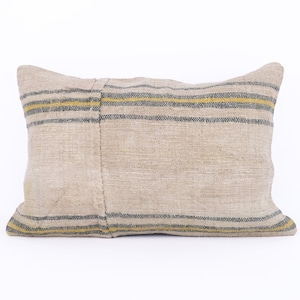 Puede incluir: Una almohada beige con rayas azules y amarillas. La almohada está hecha de tela tejida y tiene un aspecto rústico.