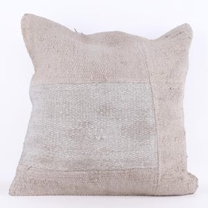 May include: A square, off-white throw pillow with a woven texture. The pillow has a large, rectangular patch of a lighter shade of white in the center.