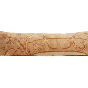 May include: A long, rectangular lumbar pillow featuring a tan background with a woven tapestry-style pattern. The design includes symmetrical depictions of birds facing each other, surrounded by floral motifs in shades of brown and muted orange.