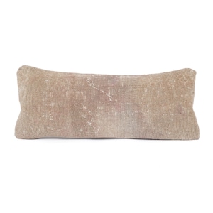 May include: A rectangular lumbar pillow featuring a weathered, muted beige and taupe textile cover. The fabric displays a distressed, worn-in texture with subtle variations in color and faint, faded linear patterns across the surface.