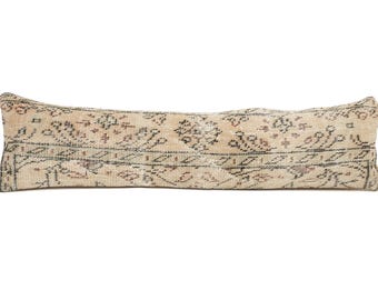 May include: A long, rectangular pillow with a beige background and a patterned design in black, red, and brown. The pillow has a vintage, distressed look, suggesting it may be an antique or a reproduction of an antique.