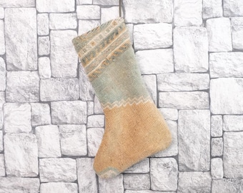 May include: A handmade Christmas stocking in beige, green, and tan. It has a patterned cuff and a zig-zag design separating the cuff from the body. The stocking is made of a woven material, perfect for festive decorations.